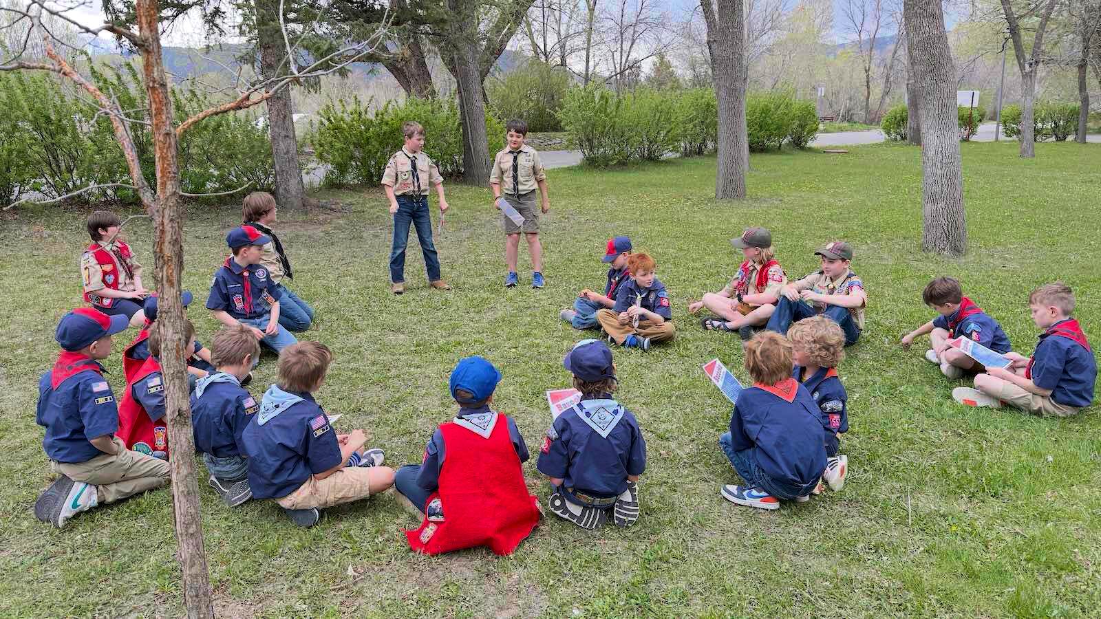 Cub Scouts from across the pack sitting in a circle on the grass at an outdoor meeting